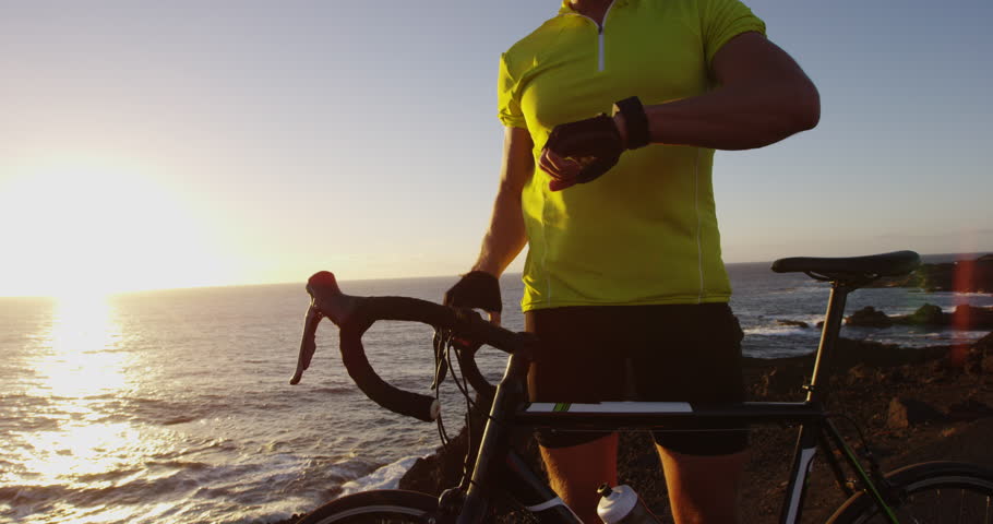 Cyclist biking looking at smartwatch while cycling riding road bike. Athlete biker using activity tracker gps fitness watch on workout at sunset. Sports man using his watch app for fitness tracking. Royalty-Free Stock Footage #34428868
