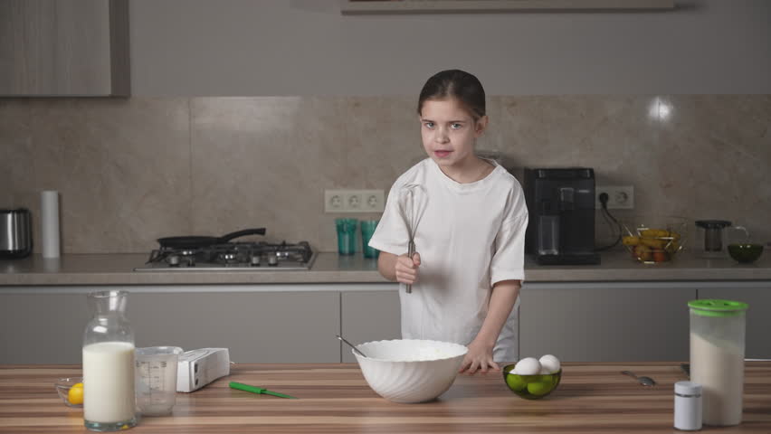 Girl having fun, dancing, singing karaoke and enjoying time on family kitchen at home on women's day. Smiling child cooking, making dough for pancakes for breakfast. Royalty-Free Stock Footage #3442897527