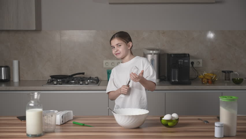 Girl having fun with whisk, looking to camera, smiling and enjoying time on family kitchen at home on women's day. Child cooking, making dough for pancakes for breakfast. Royalty-Free Stock Footage #3442904725