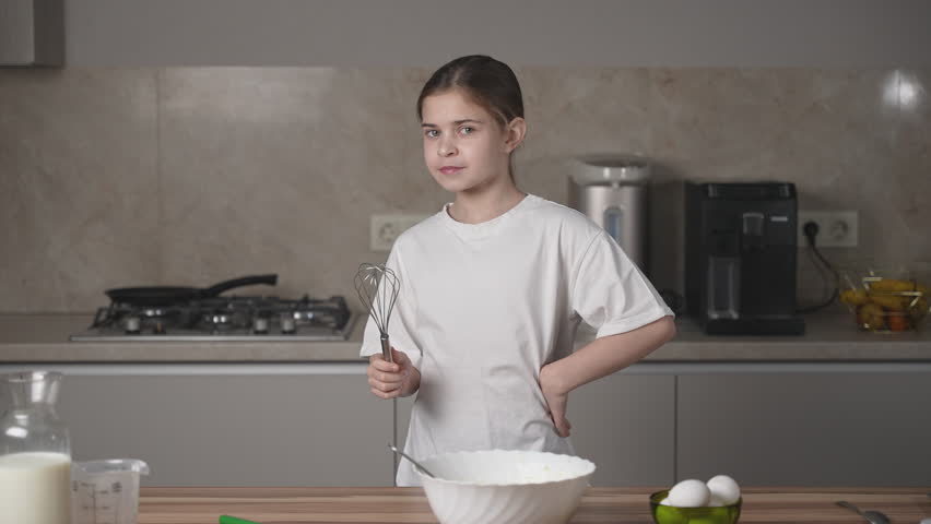 Portrait of girl having fun with whisk, looking to camera, smiling and enjoying time on family kitchen at home on women's day. Child cooking, making dough for pancakes for breakfast. Royalty-Free Stock Footage #3442909217