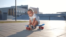 baby rides sitting on skateboard. happy family kid dream concept. baby son learning to skateboard playing funny video. child in a skate park rides a skateboard lifestyle outdoors