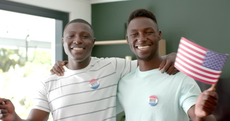 African American friends celebrate at home, wearing vote badges with American flags. They wear \"I Voted\" stickers, highlighting their civic engagement, slow motion.