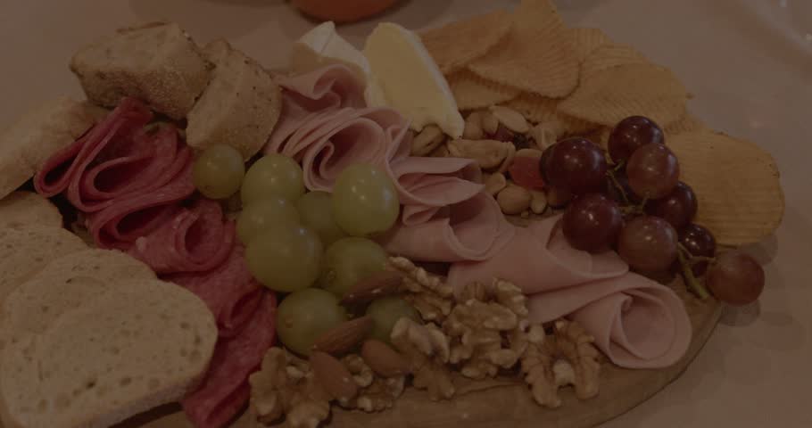 Various snacks - cheese and meat boards, nuts and olives, fish, chips, crackers and bread. White wine and rose, fruits and berries. A table with snacks against the backdrop of a fireplace with candles