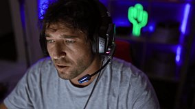 Focused man with headphones and microphone in a neon-lit gaming room at night.