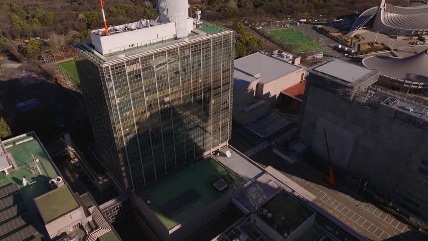 High angle view of multistorey building with antennas on top. Tilt up revealing large lark and skyline with downtown skyscrapers. Tokyo, Japan