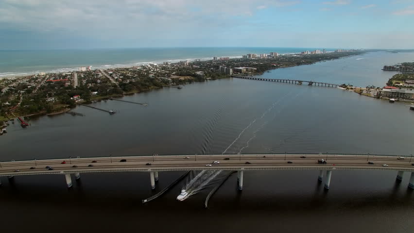 Aerial Tilt Down Shot Of Motorboat Moving Under Segmental Bridge In Residential City, Drone Flying Forward On Sunny Day - Daytona Beach , Florida