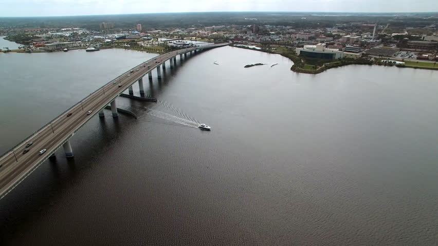 Aerial Panning Shot Of Motorboat Moving Under Segmental Bridge In Residential City On Sunny Day - Daytona Beach , Florida