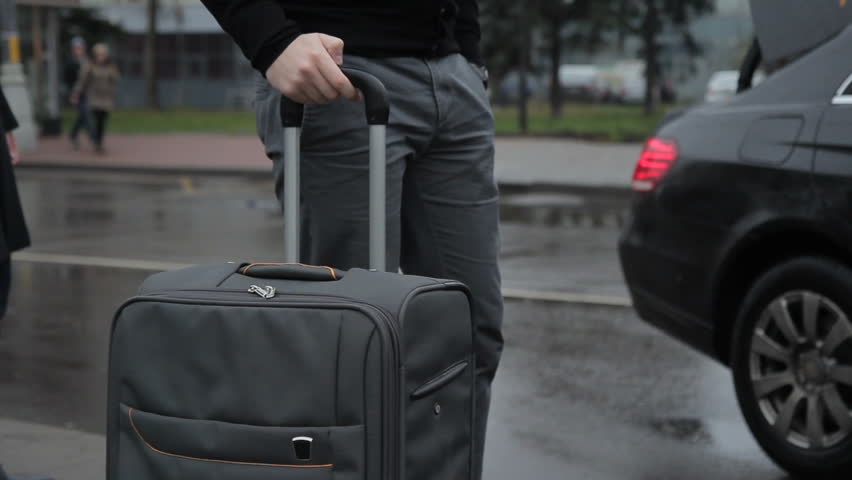 Man is loading large suitcase with handle in trunk of car. In rainy weather driver of car removes luggage from person in coat in transport section. | Shutterstock HD Video #34431040