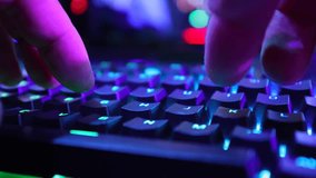 Close up view of hands typing RGB gaming keyboard, with dynamic colorful backlighting in a dark gaming environment. Slow Motion, 4K RAW. 