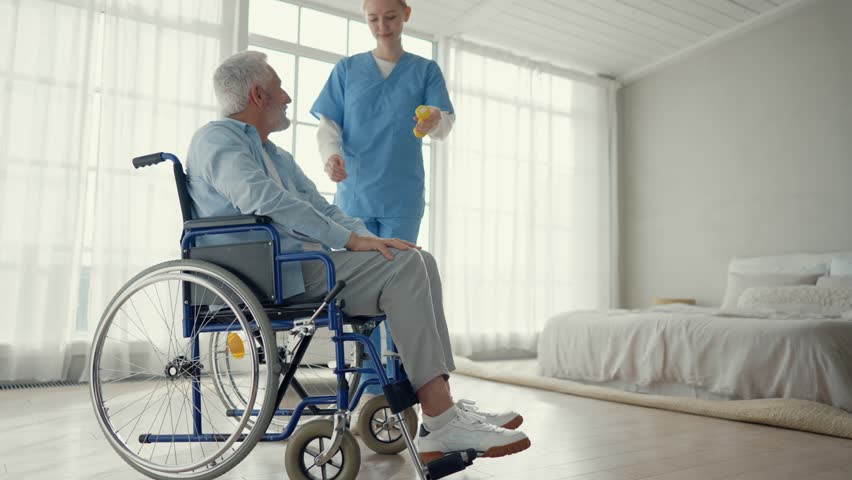 Man in wheelchair exercising with nurse. Social medical worker woman helping special needs male doing hands exercises with dumbbell. Palliative care in late stage of neurodegenerative pathologies. Royalty-Free Stock Footage #3443312841