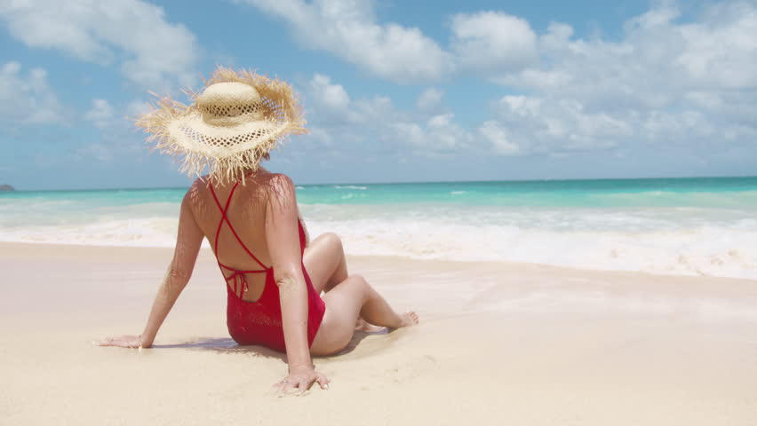 Beautiful girl in straw hat and red swimsuit enjoying sunbath at beach. Back view young tanned woman enjoying breeze at azule blue ocean background. Carefree woman smiling, throwing head back Hawaii Royalty-Free Stock Footage #3443341587