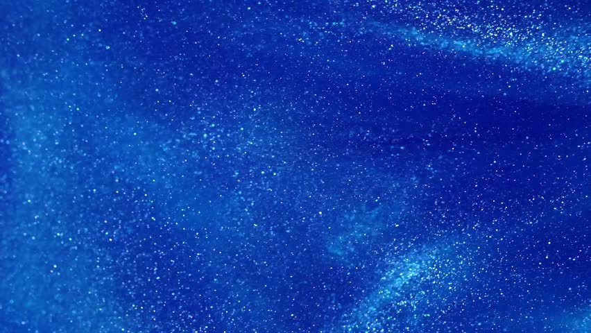 A vortex of white particles slowly unfolding against a blue background. White glowing dust particles overflows in blue liquid. Magic snowy galaxy background.