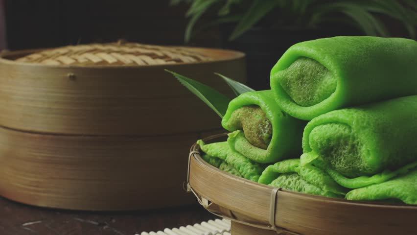 Indonesian snack. Close up of ‘Kue Dadar Gulung’ on bamboo plate with teapot as a background. It made from flour, coconut, palm sugar and pandanus flavors. Selective focus. 