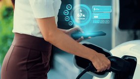 Modern lifestyle woman insert EV charger to his electric car at home charging station and check EV battery status hologram from smartphone. Futuristic energy sustainability and electric car. Peruse - Powered by Shutterstock - Get 15% off with code: PIKWIZARD15