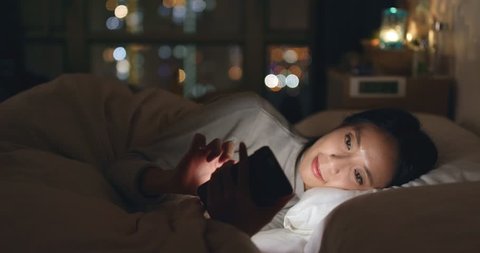 Woman sending sms on cellphone and lying on bed