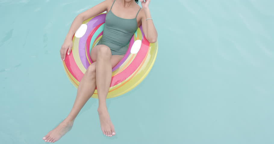 Young biracial woman enjoys a swim on a colorful float, with copy space. She's relaxing in a pool, creating a serene summer vibe, slow motion. Royalty-Free Stock Footage #3443529867