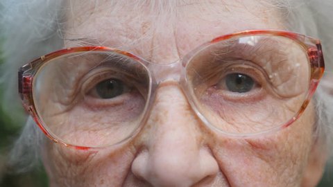 Old woman in eyeglasses looking into camera. Slow motion