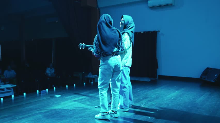 Two people on stage with one holding a guitar, backlit by stage lights during the night