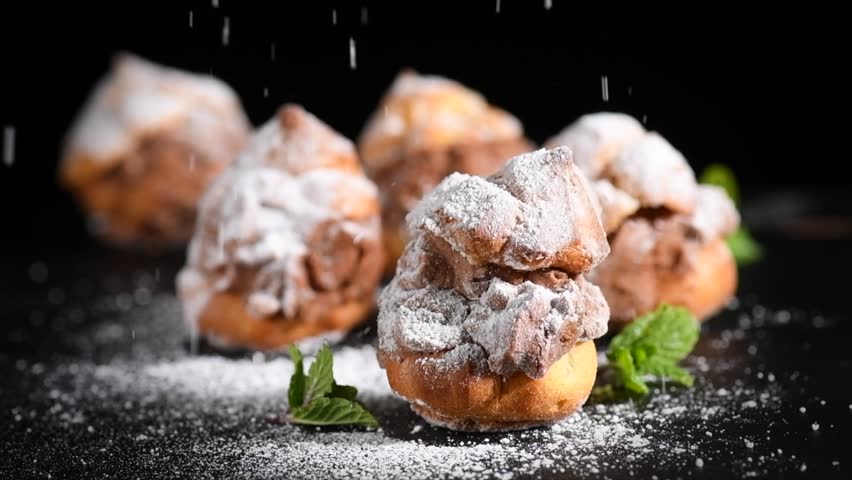Profiteroles or cream puff with filling,  falling powder sugar topping. Berries, mint on black background. Fresh homemade Cream Puffs, cake, tasty French choux puff, ecler, dessert closeup. Pastries