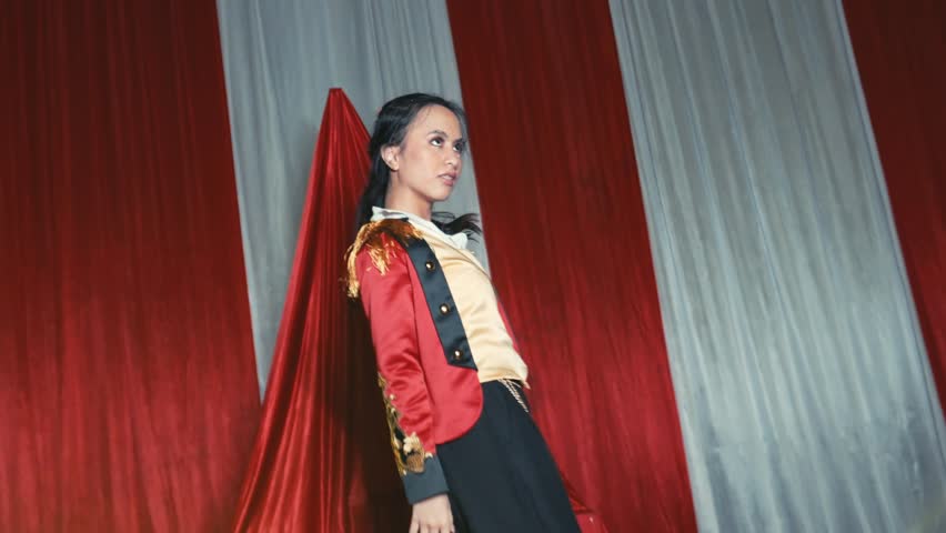 Person in pirate costume posing playfully with a sword on a theatrical stage with red curtains during the night