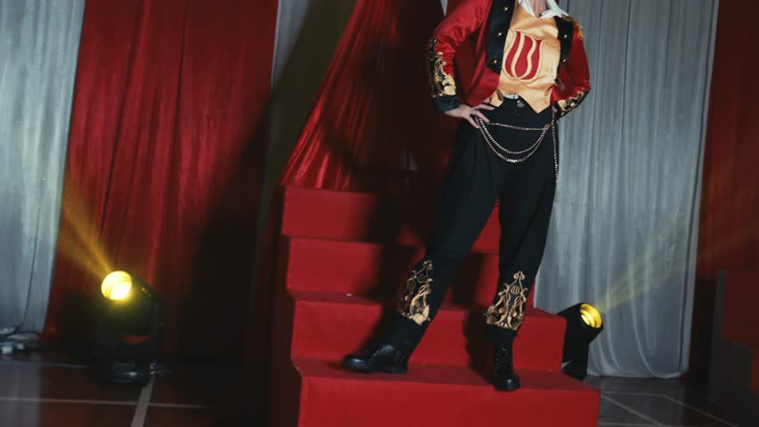 Confident woman in a red and black costume with a dramatic fiery effect on stage, curtains in the background during the night