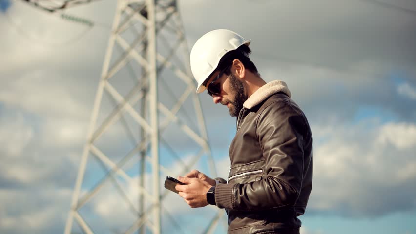 Constructor Inspect High Voltage Tower.Engineer In Hard Hat Maintenance Electricity Transmission Pylon.Electrical Engineer In Helmet Power Line.Constructor Checking High Voltage Sensor Power Line Wire