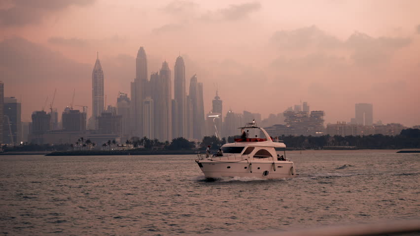 Luxury yacht sailing in Dubai UAE during sunset with skyscrapers and scenic clouds in the background