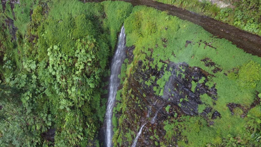 Steep cliff waterfall flows onto narrow mountain dirt road in Bolivia