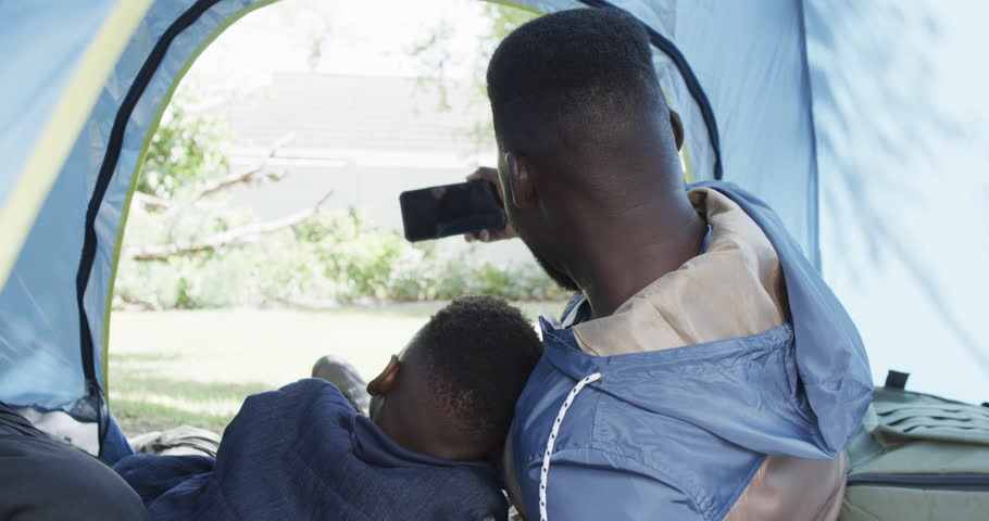 African American father and son enjoy time in a tent outdoors. They share a bonding moment while camping in the backyard, slow motion.