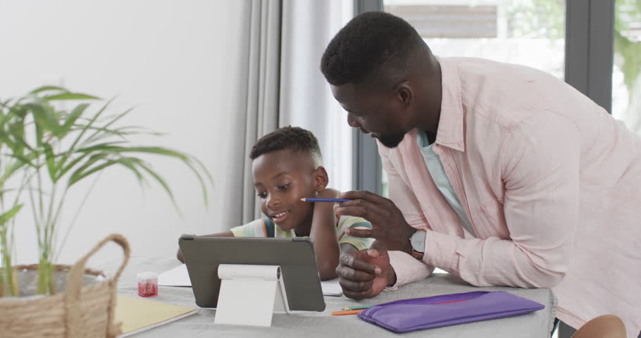 African American father helps a son with homework at home using a tablet. They focus intently on the device, suggesting a modern approach to learning and education, slow motion. Royalty-Free Stock Footage #3443808307