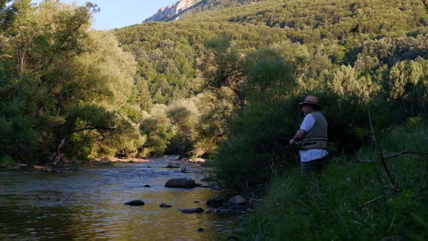 Man fishing in the mountain river that is flowing through the forest in the golden hour