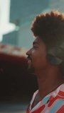 VERTICAL VIDEO, Close-up of cheerful young man wearing shirt listening to music in headphones and dancing on urban city background. Lifestyle concept. Backlight Slow motion