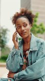 VERTICAL VIDEO, Beautiful girl with ponytail wearing denim jacket talking on mobile phone on modern city background. Slow motion