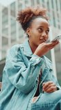 VERTICAL VIDEO,Close-up portrait of girl with ponytail wearing denim jacket leaving voice message on mobile phone against modern city background. Slow motion