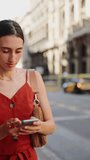 VERTICAL VIDEO: Beautiful young woman walks and looks at a map on a mobile phone. Closeup of romantic girl goes through the downtown and looks into the smartphone.