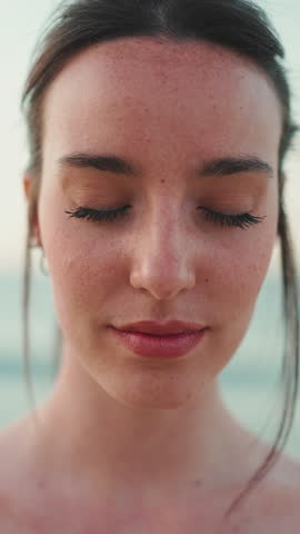 VERTICAL VIDEO: Close-up young athletic woman with long ponytail wearing beige sports top is standing eyes closed and relaxing on the sea background Royalty-Free Stock Footage #3443914905