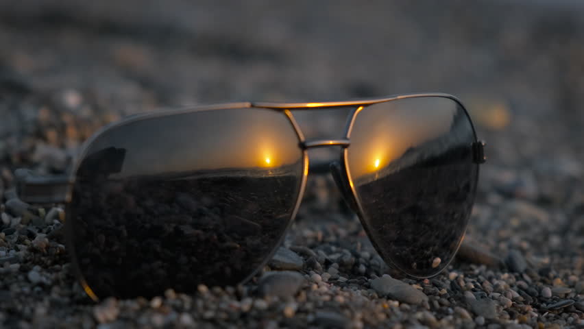 Sunglasses left on shore. A black sunglasses with ocean waves reflection on pebbles under sun rays. Royalty-Free Stock Footage #3443915821
