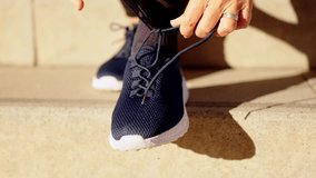 Video close-up of a mature woman tying her running shoes sitting on stairs