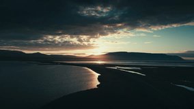 Incredible and epic drone and aerial shot of the setting sun against a bridge and series of lakes with mountains in the distance. The camera tracks forward.