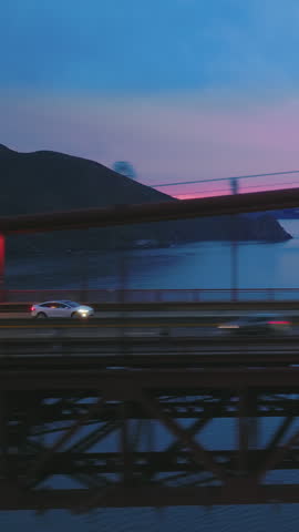 Vertical video. Aerial view of magnificent red suspension Golden Gate Bridge with traffic with cinematic pink sunset on motion background. US route 101 on road bridge full of cars with headlights.