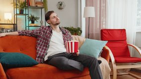 Excited man eating popcorn watching interesting tv serial sport game online social media movie content sitting on sofa in room at home. Happy Caucasian guy in plaid shirt enjoying film during weekend - Powered by Shutterstock - Get 15% off with code: PIKWIZARD15