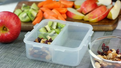 Woman hand put healthy fruit and nut snacks into the lunch box and close it