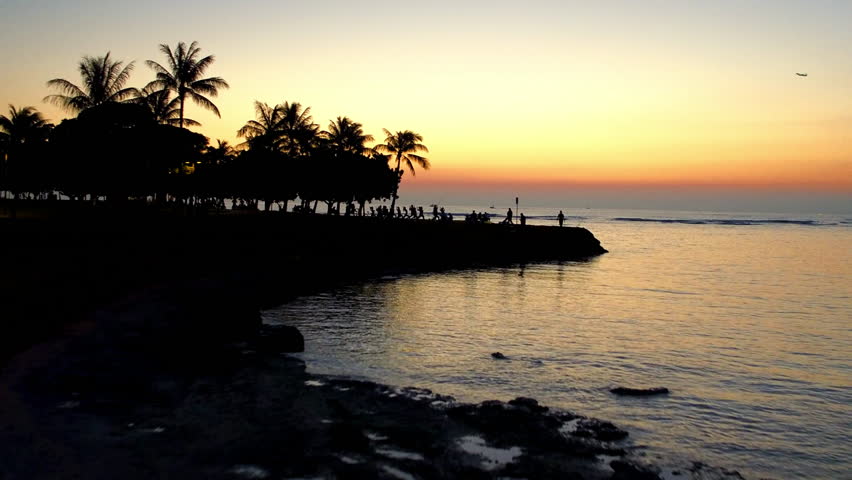 Aerial Shot Of Silhouette Of People In Park On Weekend, Drone Flying Forward Over Wavy Sea At Sunset - Honolulu, Hawaii