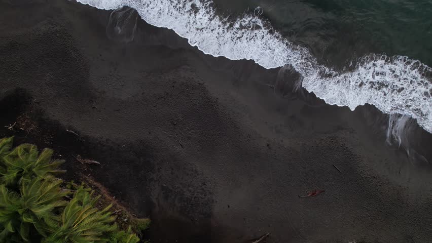 Foamy Waves Splashing On The Black Sand Beach Of Grand Anse In Guadeloupe, France - Aerial Top Down
