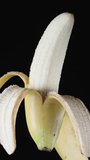 A half-peeled banana on a black background, chocolate is poured on top of it. Isolate , close-up. Vertical video Social Media