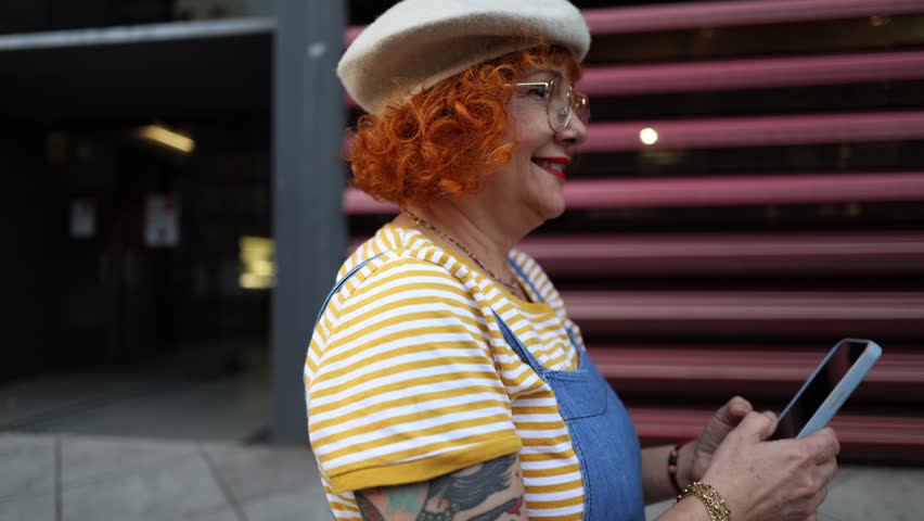 tattooed redhead mature woman walking through the city with smart phone