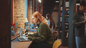 Young woman working on laptop in cozy cafe with other people engaging in conversation in background. Concentrated study in co-working space. Education and resource searching concept - Powered by Shutterstock - Get 15% off with code: PIKWIZARD15