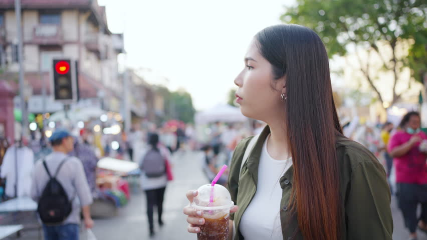 Happy Asian woman enjoy and fun outdoor lifestyle travel in Thailand on summer holiday vacation. Attractive girl walking and shopping at weekend street market and eating street food in Chiang Mai city