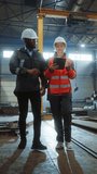 Two Heavy Industry Engineers Stand in Steel Metal Manufacturing Factory, Use Digital Tablet Computer and Have a Discussion. Black Industrial Specialist Talk to Female Technician. Vertical Screen