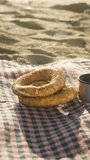 Breakfast at sunrise on the sea beach. I pour hot tea from a thermos. Bagels lie on a plaid blanket. Vertical video Social Media